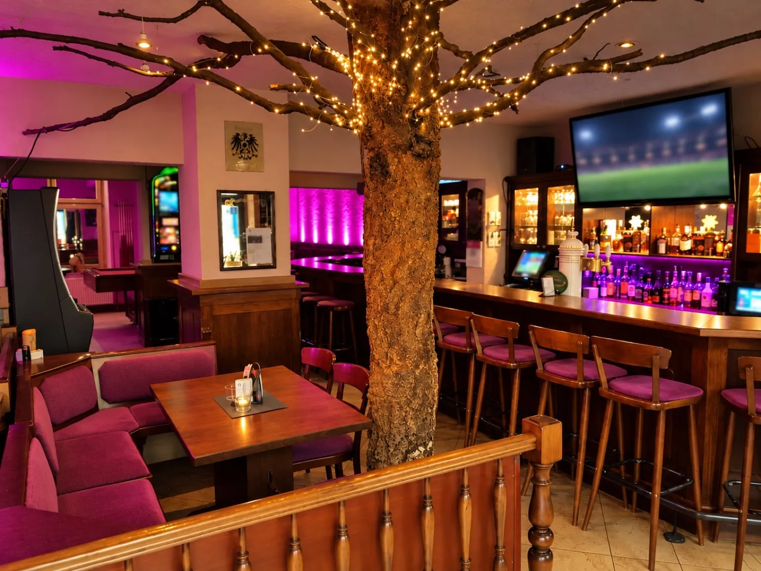 The bar room with the tree in the middle, fairy lights in the branches, bar with stools and a TV